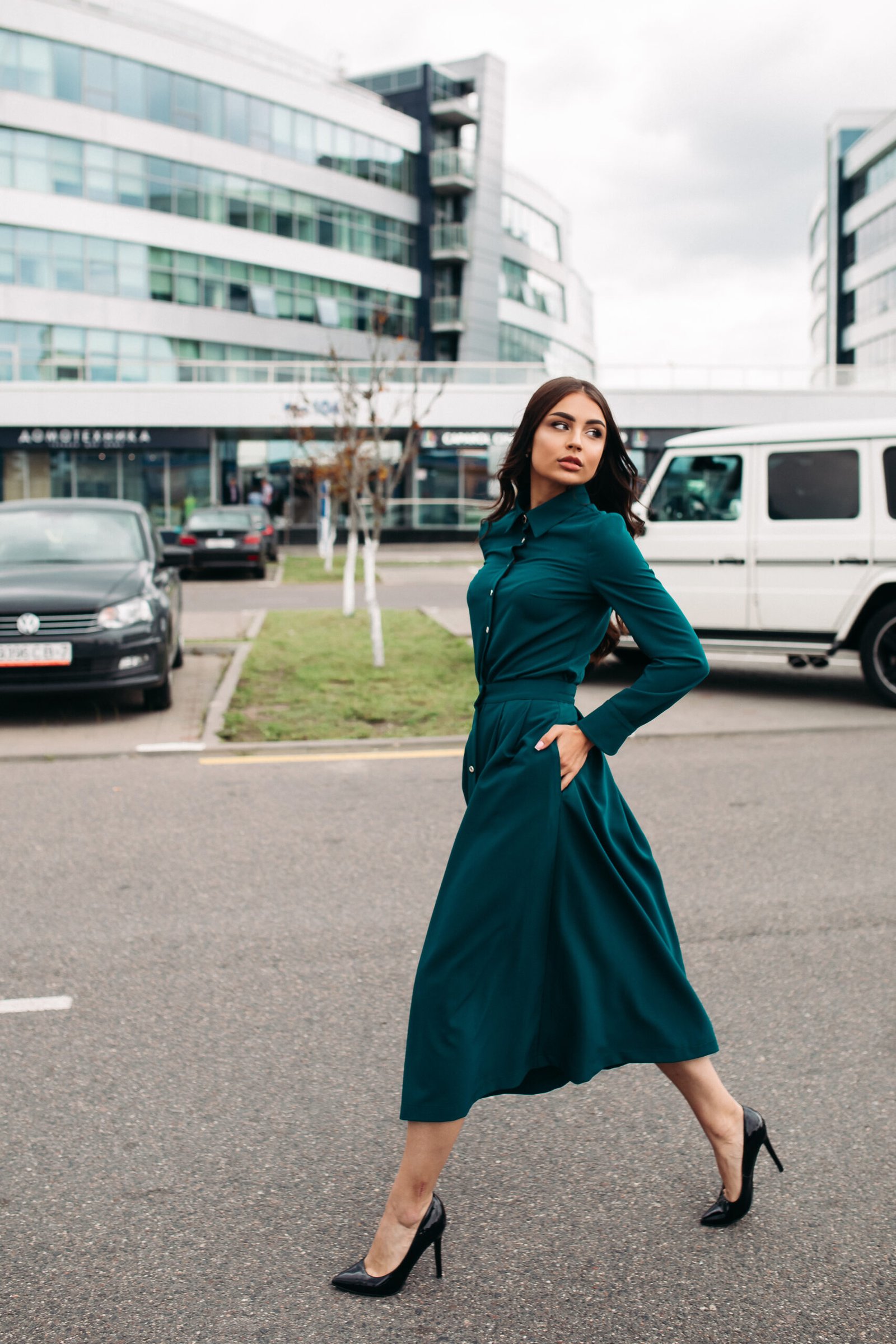 Handsome younng caucasian female with pretty face in a beautiful green dress with a length below the knee walks to the street